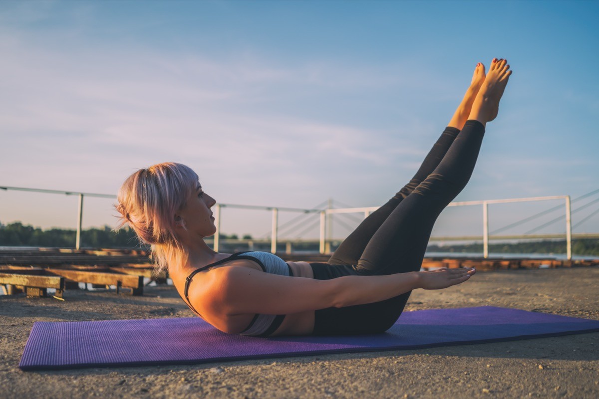 Woman exercising pilates on sunny day outside. Hundred exercise.