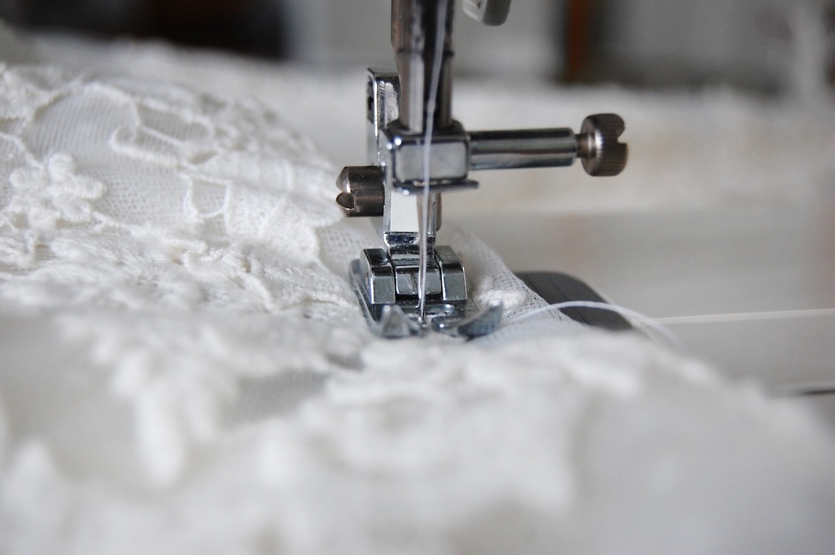 closeup of a lace wedding dress under a sewing machine