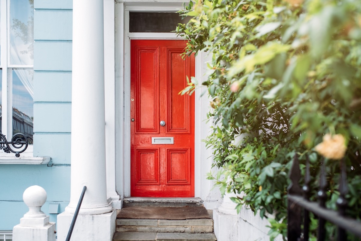 cropped image of a light blue house with a bright red door