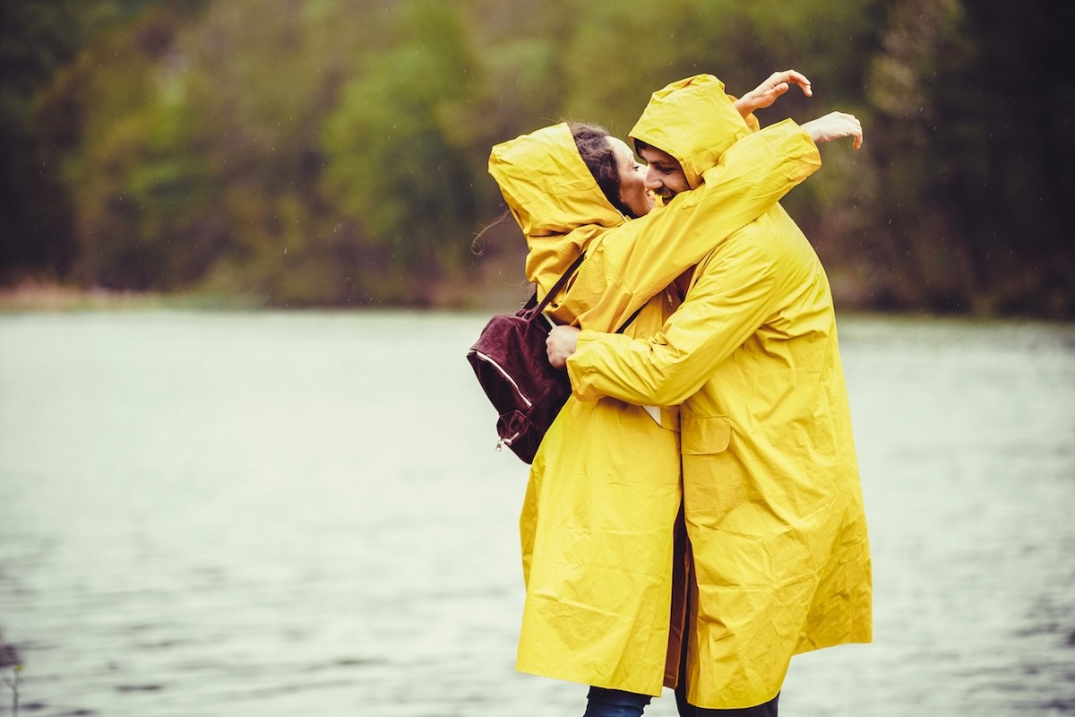 couple wearing yellow rain coats hugging and kissing next to a lake