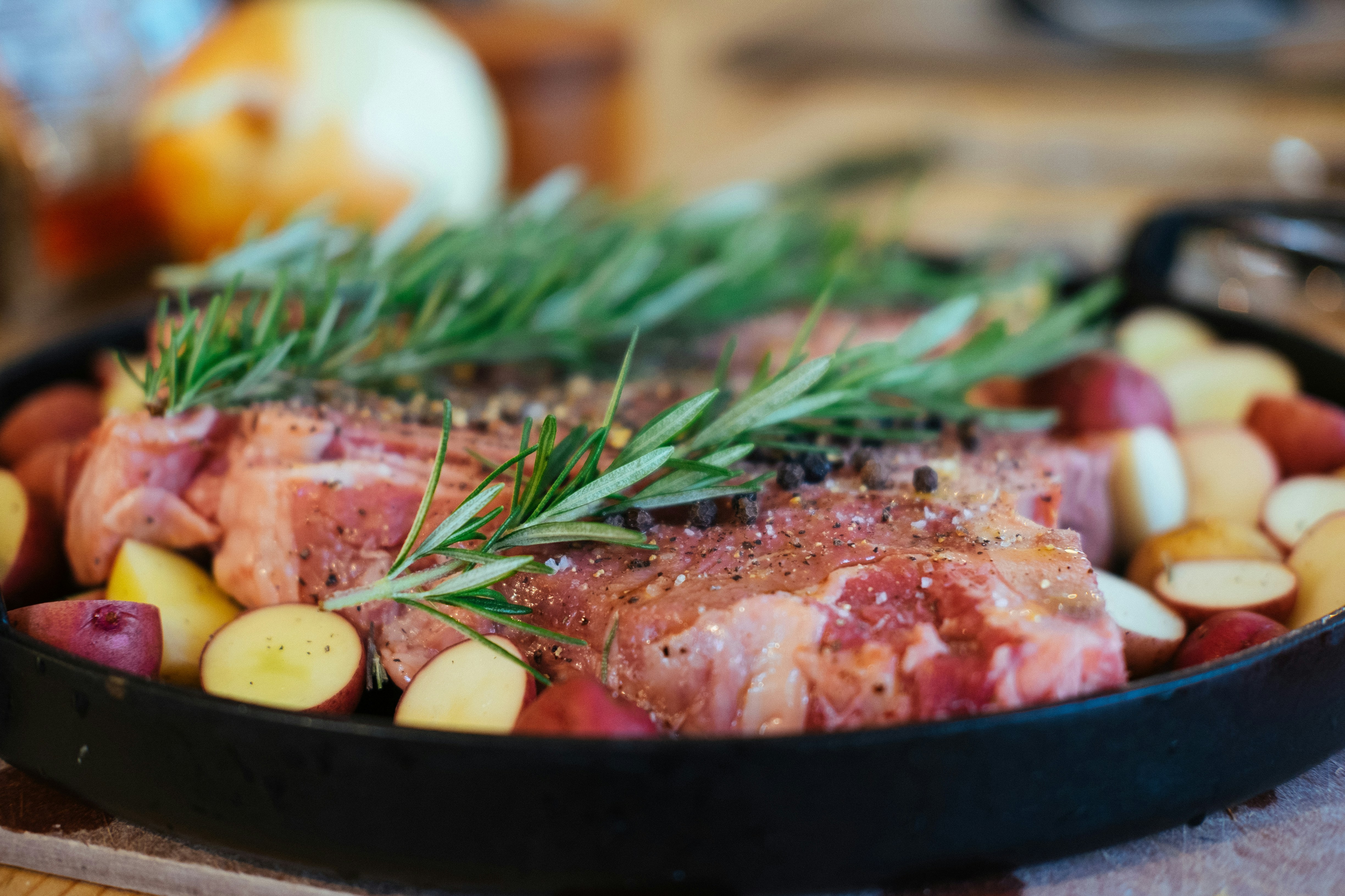 steaks with rosemary and potatoes ready to be cooked in a cast iron pan