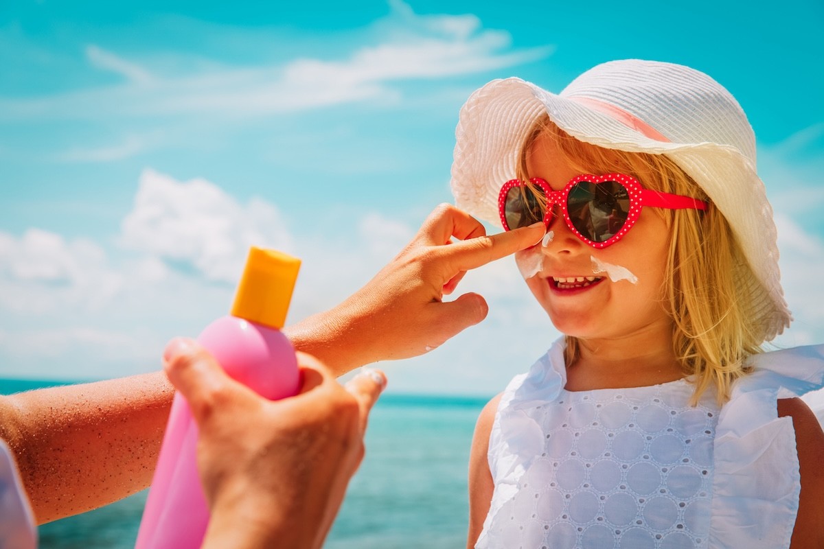 parent applying sunscreen to the face of a girl child at the beach