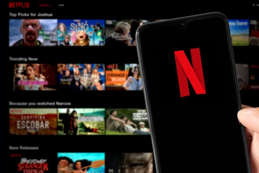 A phone with the Netflix logo on its scren in front of recommended shows and movies