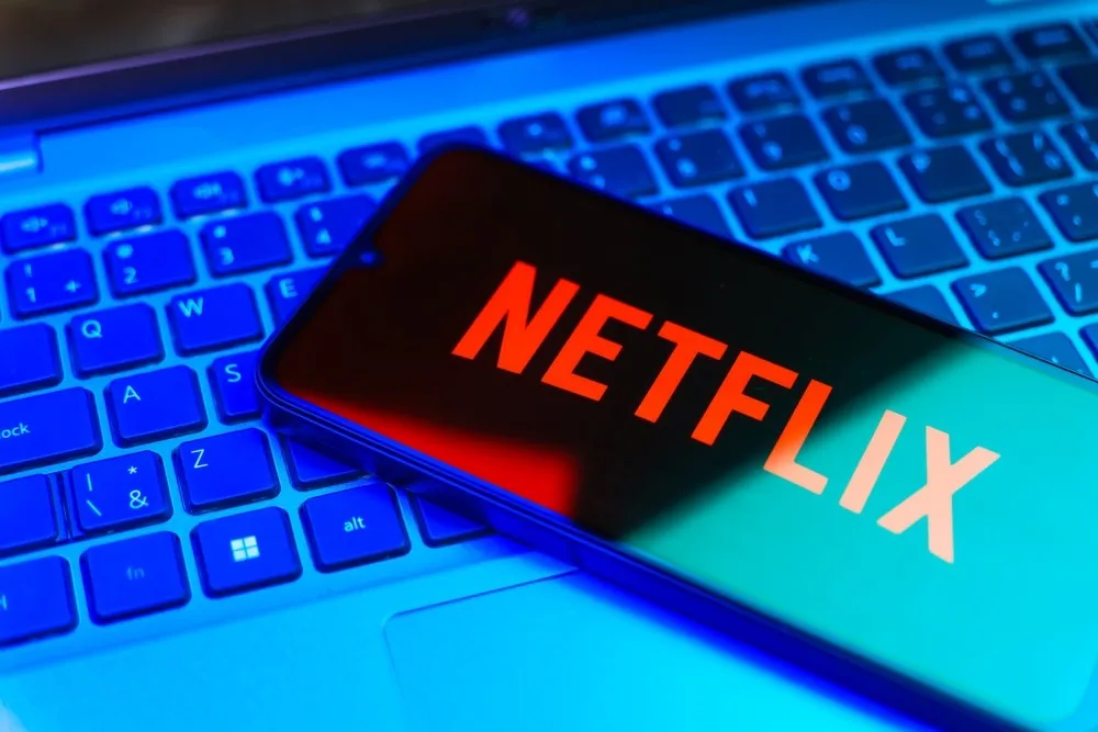 The Netflix logo on a mobile phone on top of a laptop