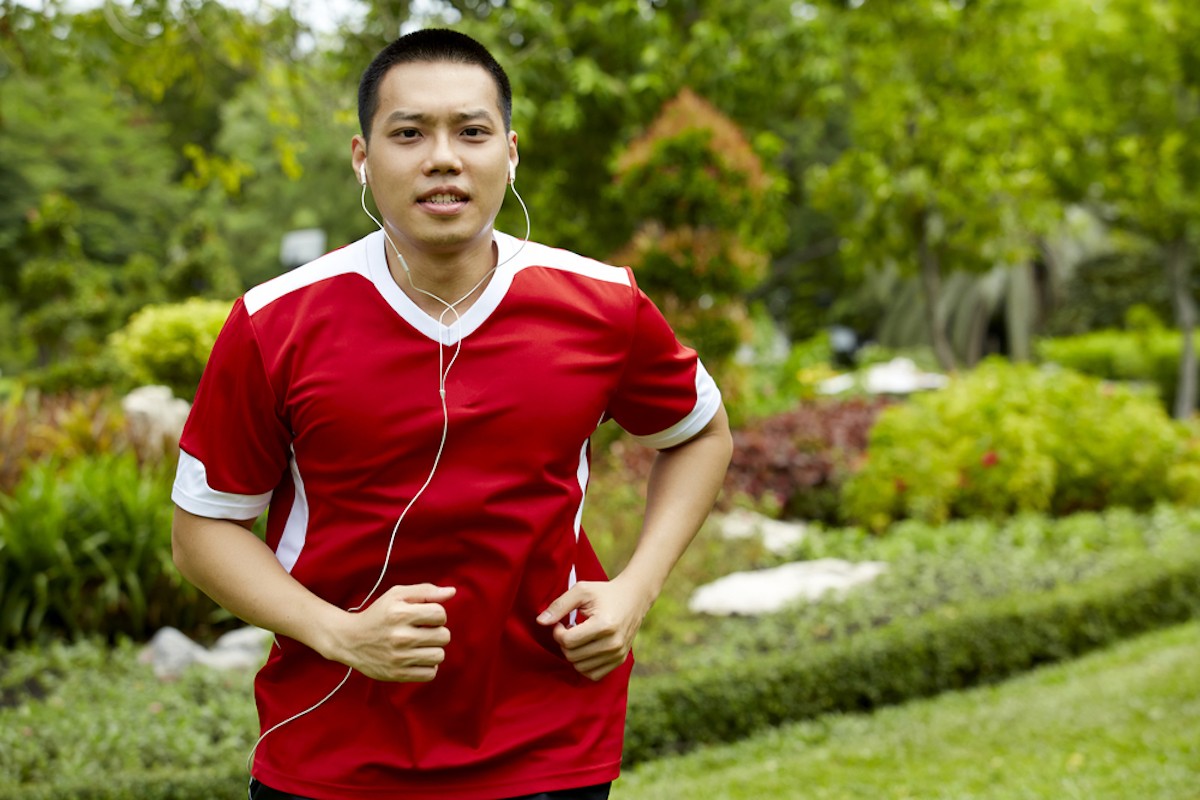 man running with headphones in ears, wearing red sports jersey shirt