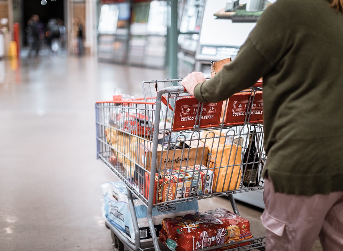 A woman pushing a shopping cart full of groceries at Costco