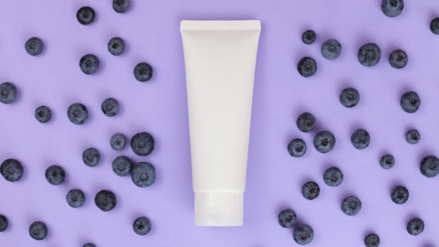 White skincare bottle surrounded by blueberries on a purple background
