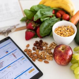 Closeup of nutritionist's desk with healthy food and digital tablet showing body mass index measurement report and nutritional plan