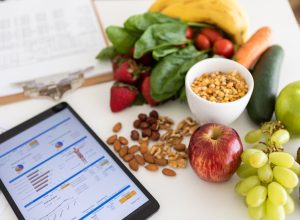 Closeup of nutritionist's desk with healthy food and digital tablet showing body mass index measurement report and nutritional plan