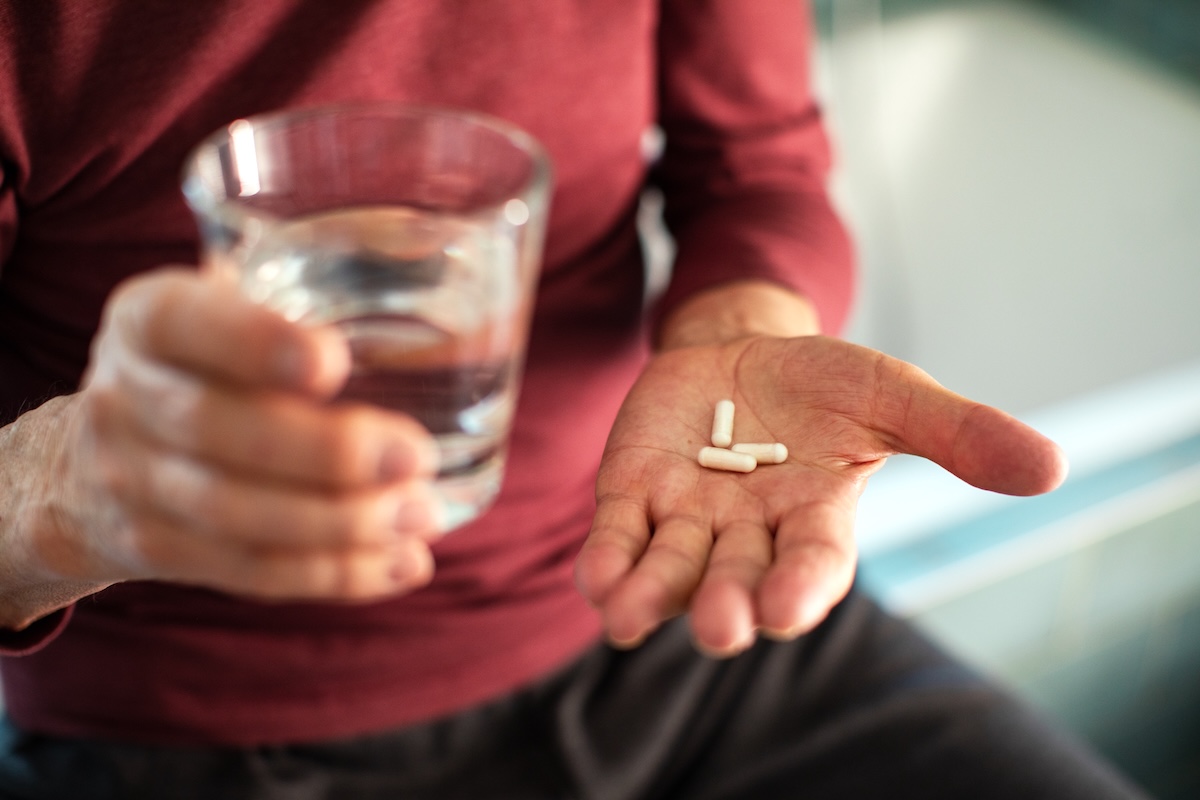 closeup of a mature man in a red shirt holding a glass of water with a few vitamins in his other hand