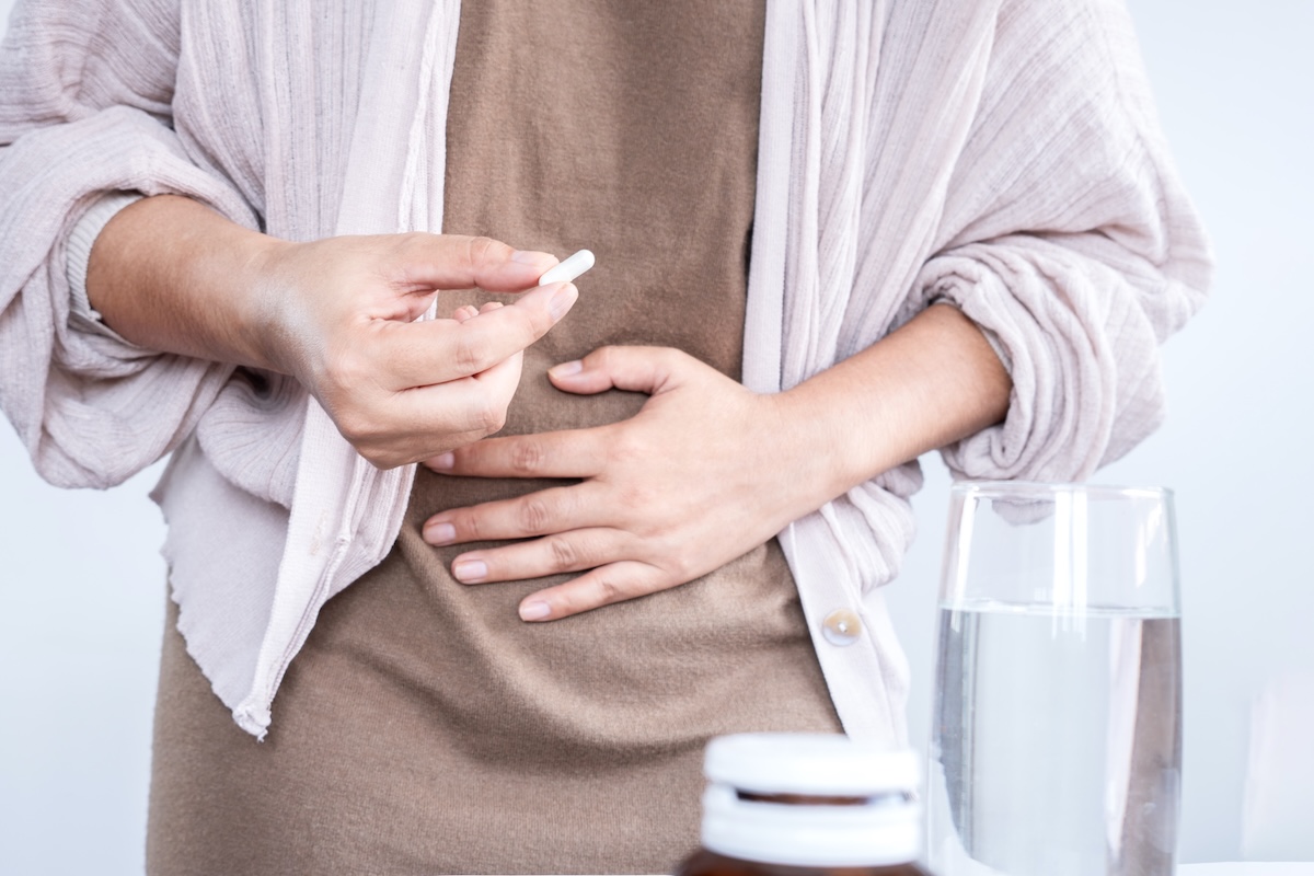 cropped image of a woman holding her stomach in pain, taking a supplement or pill