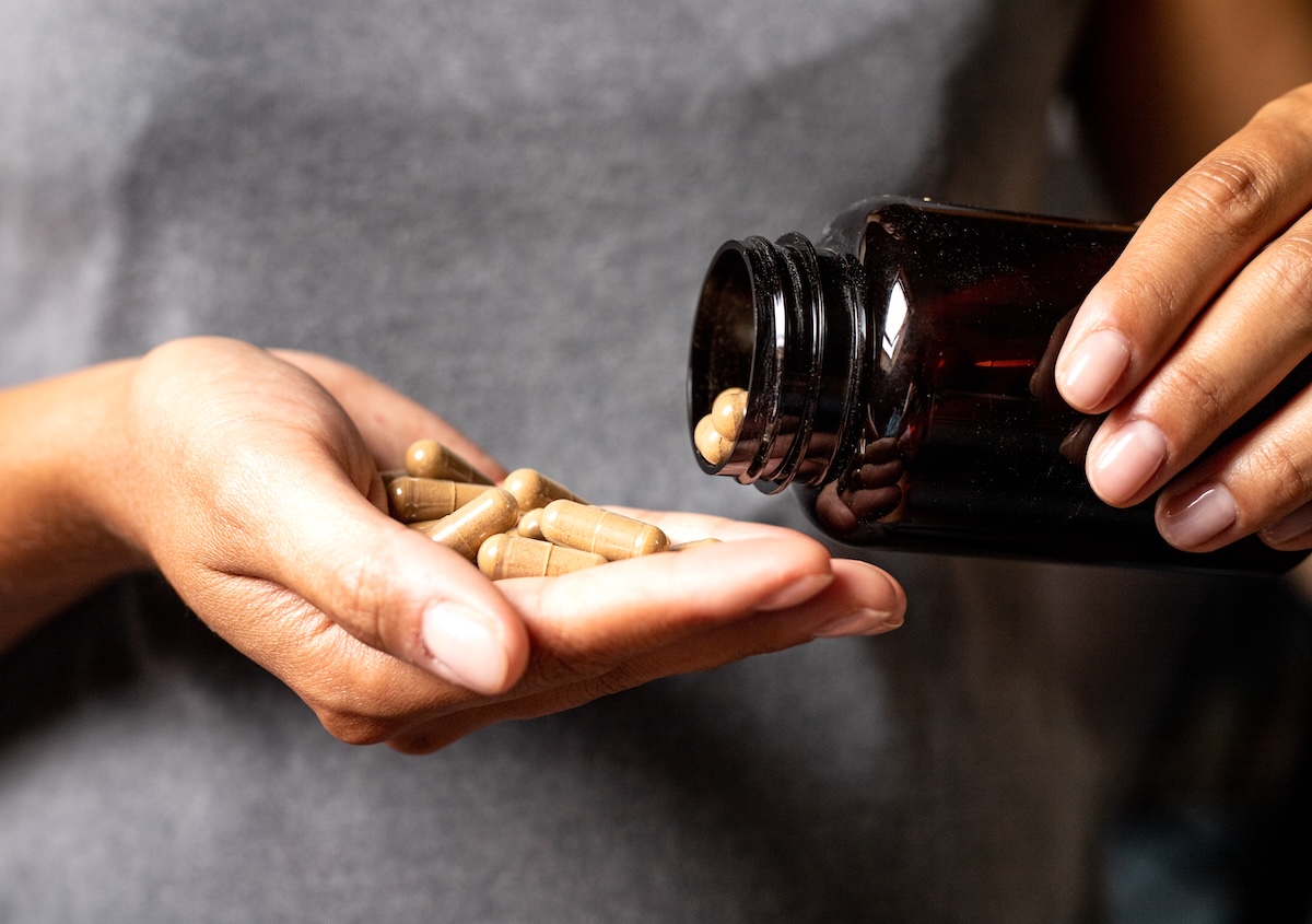 closeup of a woman in a gray t-shirt pouring supplements into her hand