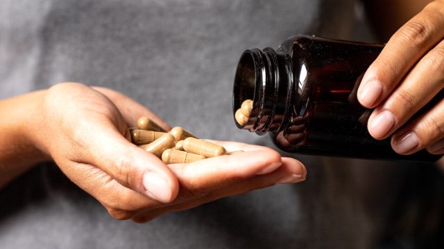 closeup of a woman in a gray t-shirt pouring supplements into her hand