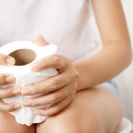 closeup of a woman clutching a roll of toilet paper while sitting on the toilet