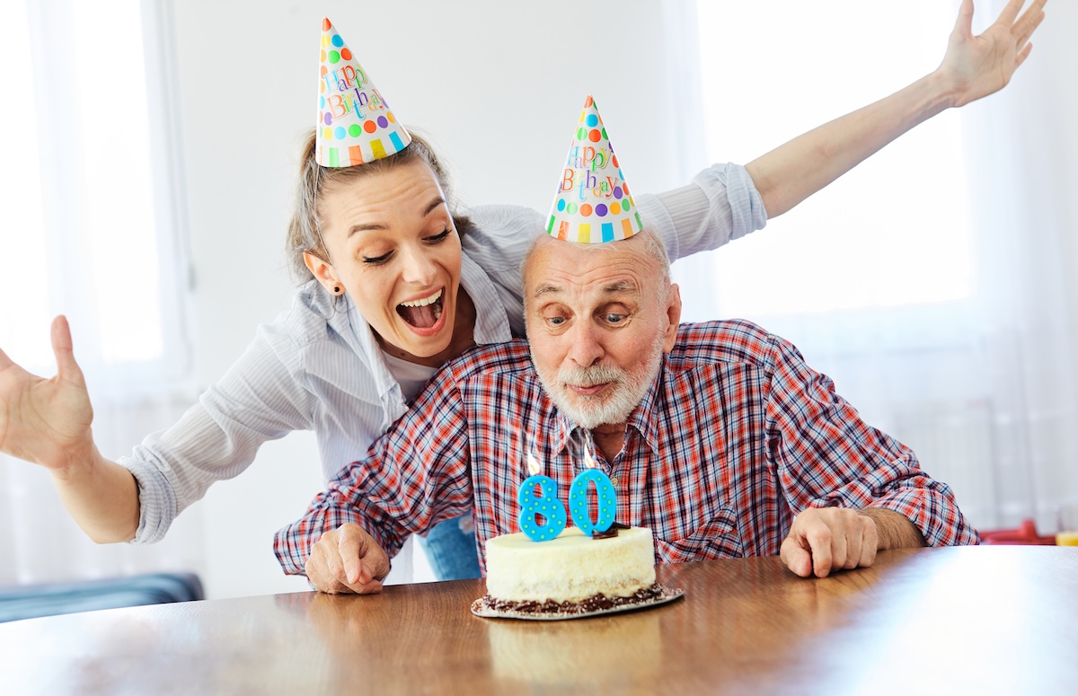 senior man and daughter celebrating his 80th birthday with party hats and a cake