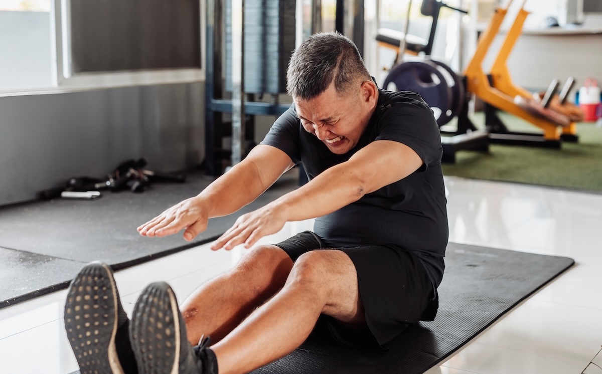 man with tight hamstrings struggling to touch his toes at the gym