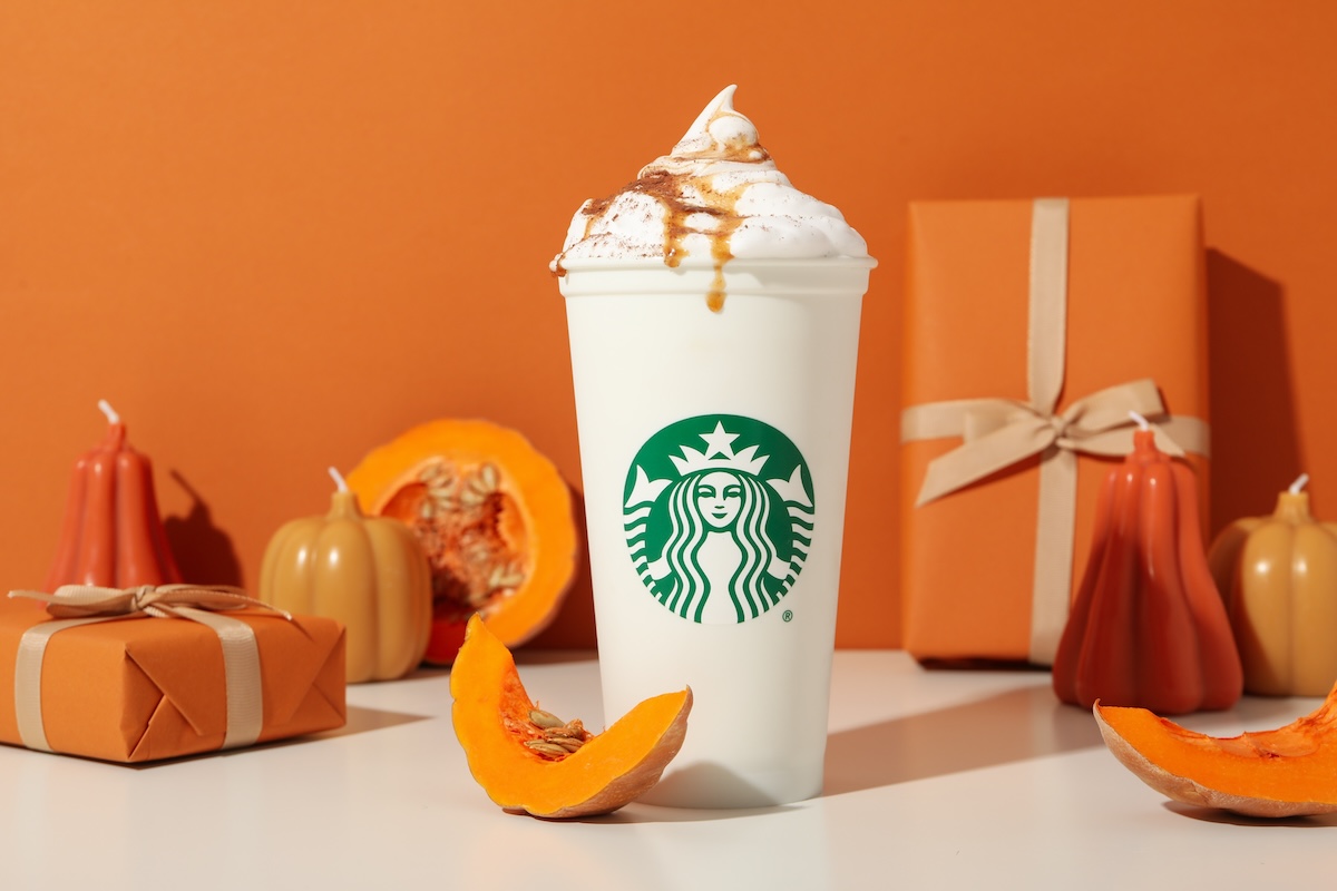 Starbucks Pumpkin Spice Latte surrounded by pumpkins and orange gifts against an orange background