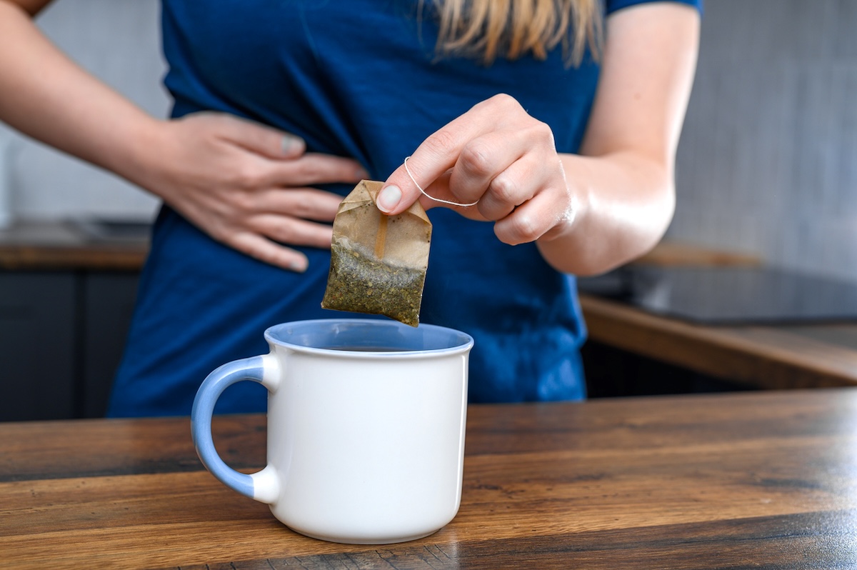 closeup of a woman with a stomach ache making a cup of tea