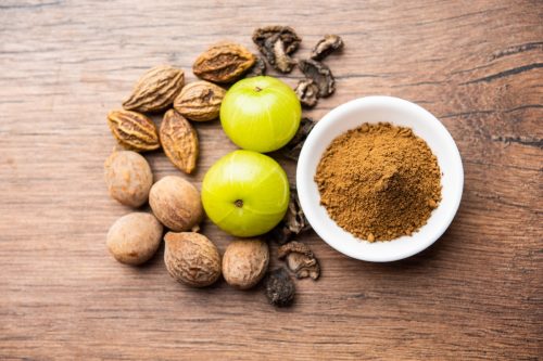 Triphala powder surrounded by Indian fruits on a wood background