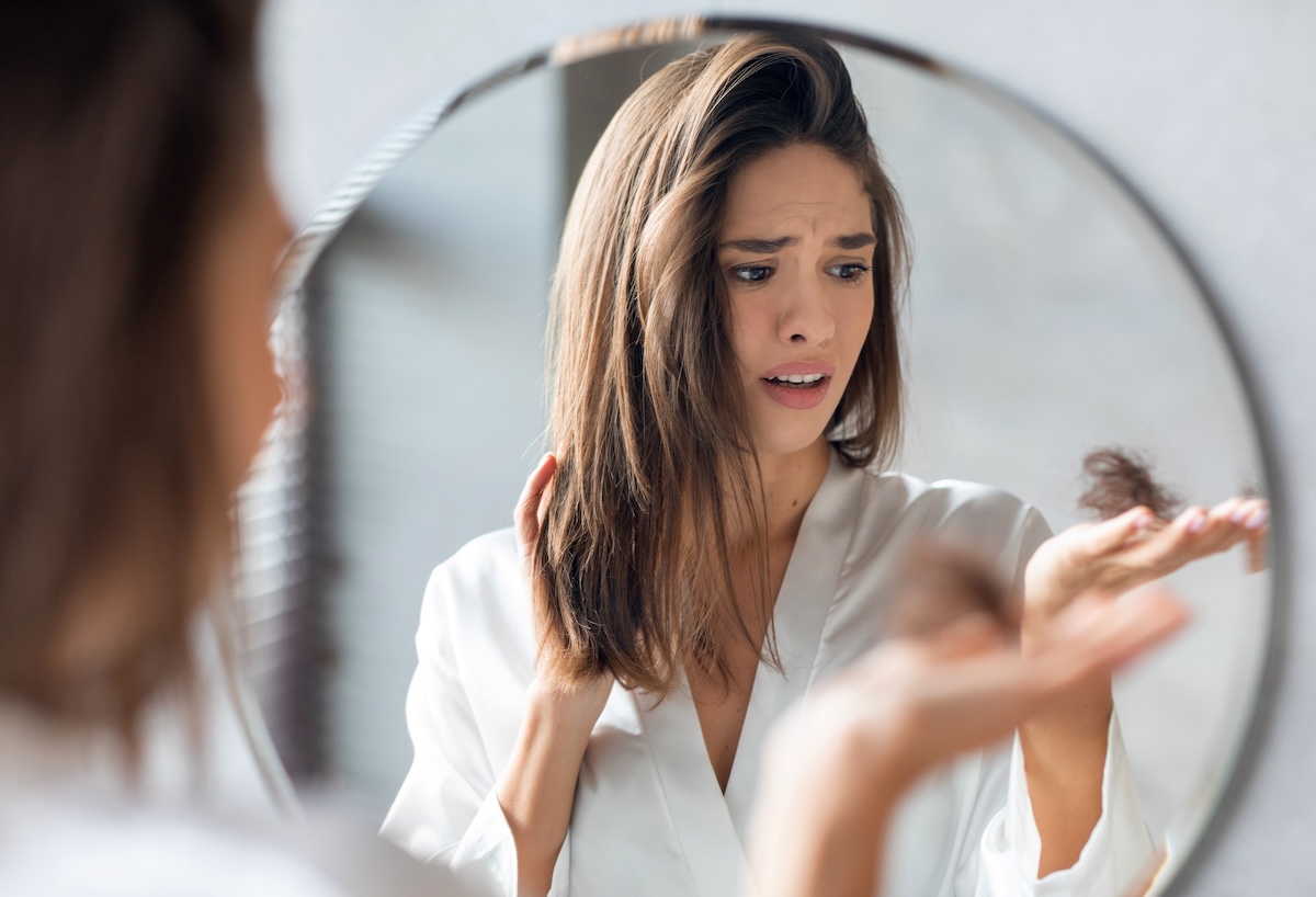 upset young woman looking in the mirror and holding a clump of hair in her hands