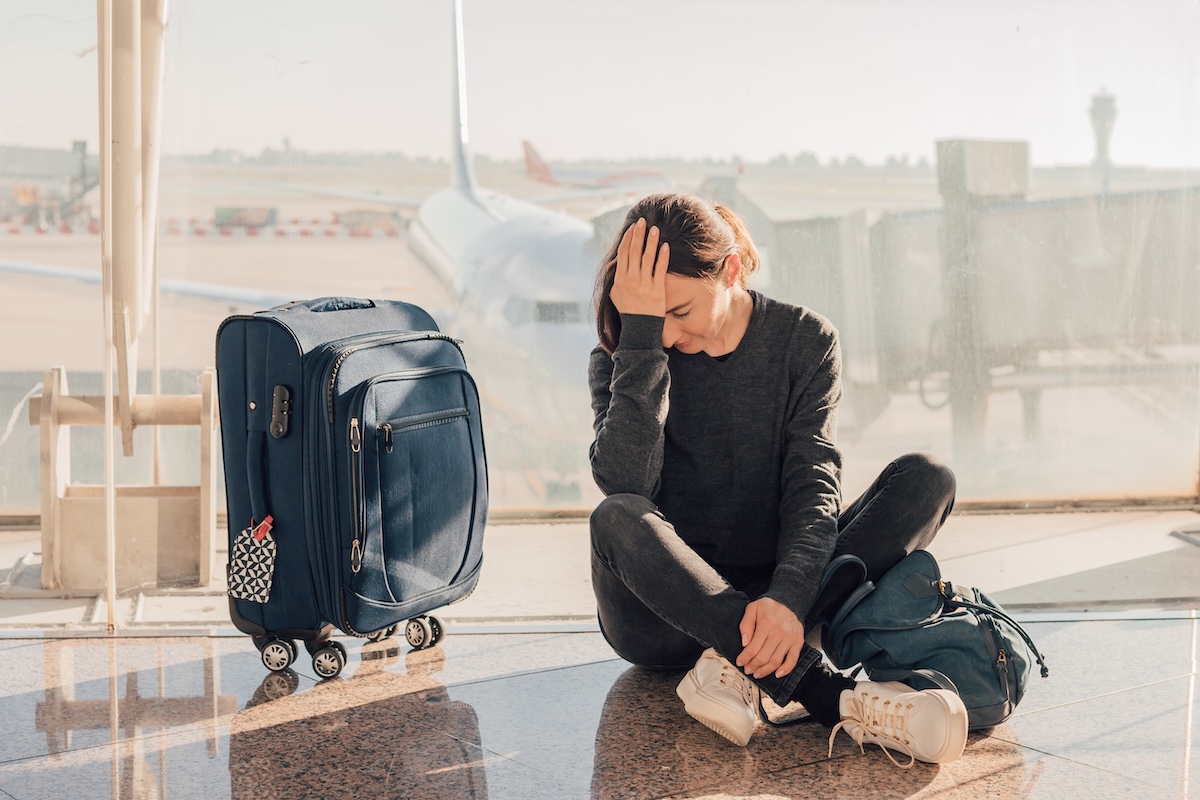 an upset woman sitting on the floor at the airport with her suitcase next to her