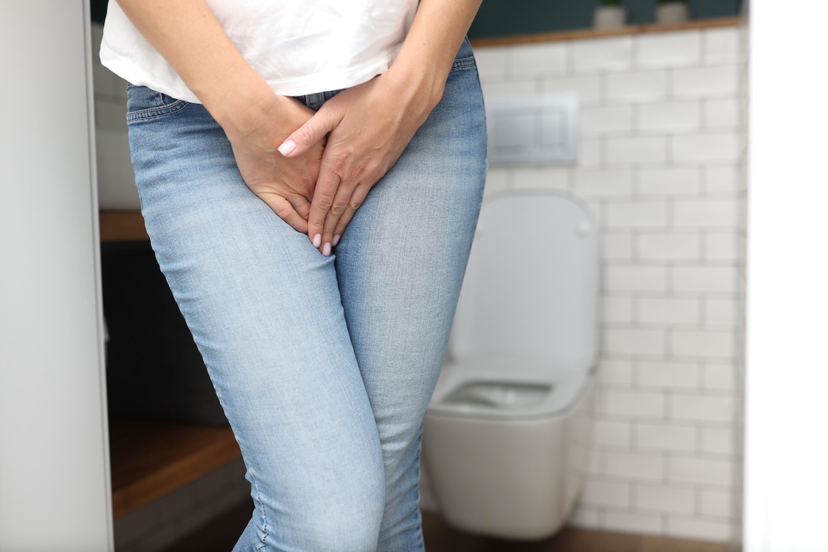 Female hands between legs in jeans close-up, showing that she has to pee