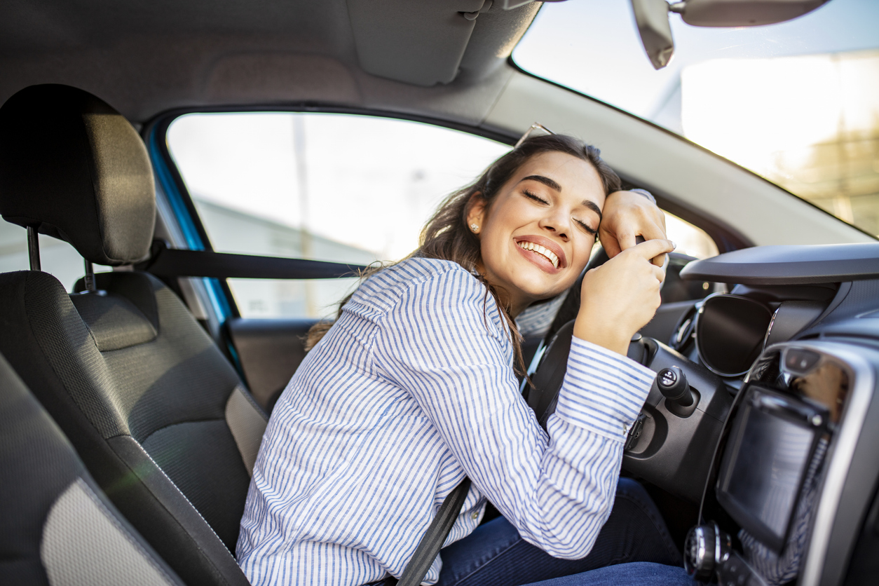 A woman hugging the steering wheel of her car and smiling
