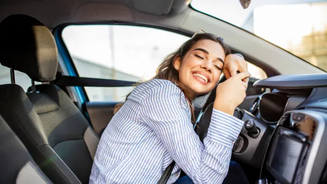 A woman hugging the steering wheel of her car and smiling