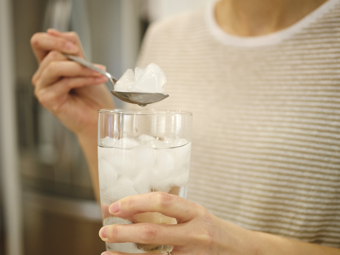 closeup of a woman in a beige sweater taking ice cubes out of a water glass with a spoon