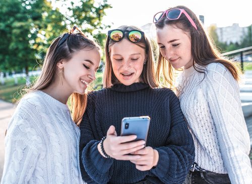 Three girlfriends girls schoolgirls teenagers 12-15 years old, autumn summer day city, read watch message phone, watch videos Internet, social networks application. Happy laughing smiling having fun.