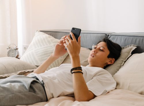 Asian boy using mobile phone while resting on bed at home