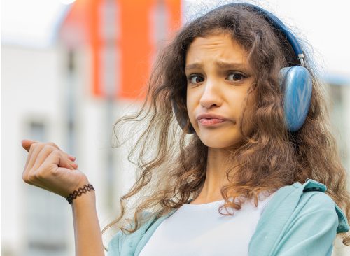 Happy relaxed overjoyed preteen child kid in wireless headphones choosing, listening favorite energetic disco rock n roll music dancing outdoors. Girl walking in urban city street background. Vertical