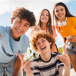 Happy smiling group of teenagers high school pupils friends classmates college students boys and girls with bags hanging out in park nature street outside take selfie shot picture photo having fun