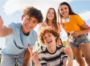 Happy smiling group of teenagers high school pupils friends classmates college students boys and girls with bags hanging out in park nature street outside take selfie shot picture photo having fun