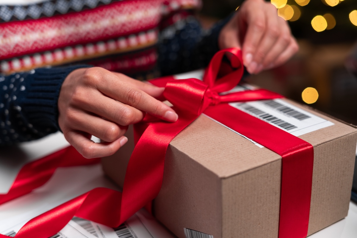 closeup of a person tying a red ribbon on a holiday package