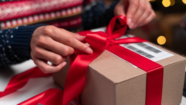 closeup of a person tying a red ribbon on a holiday package