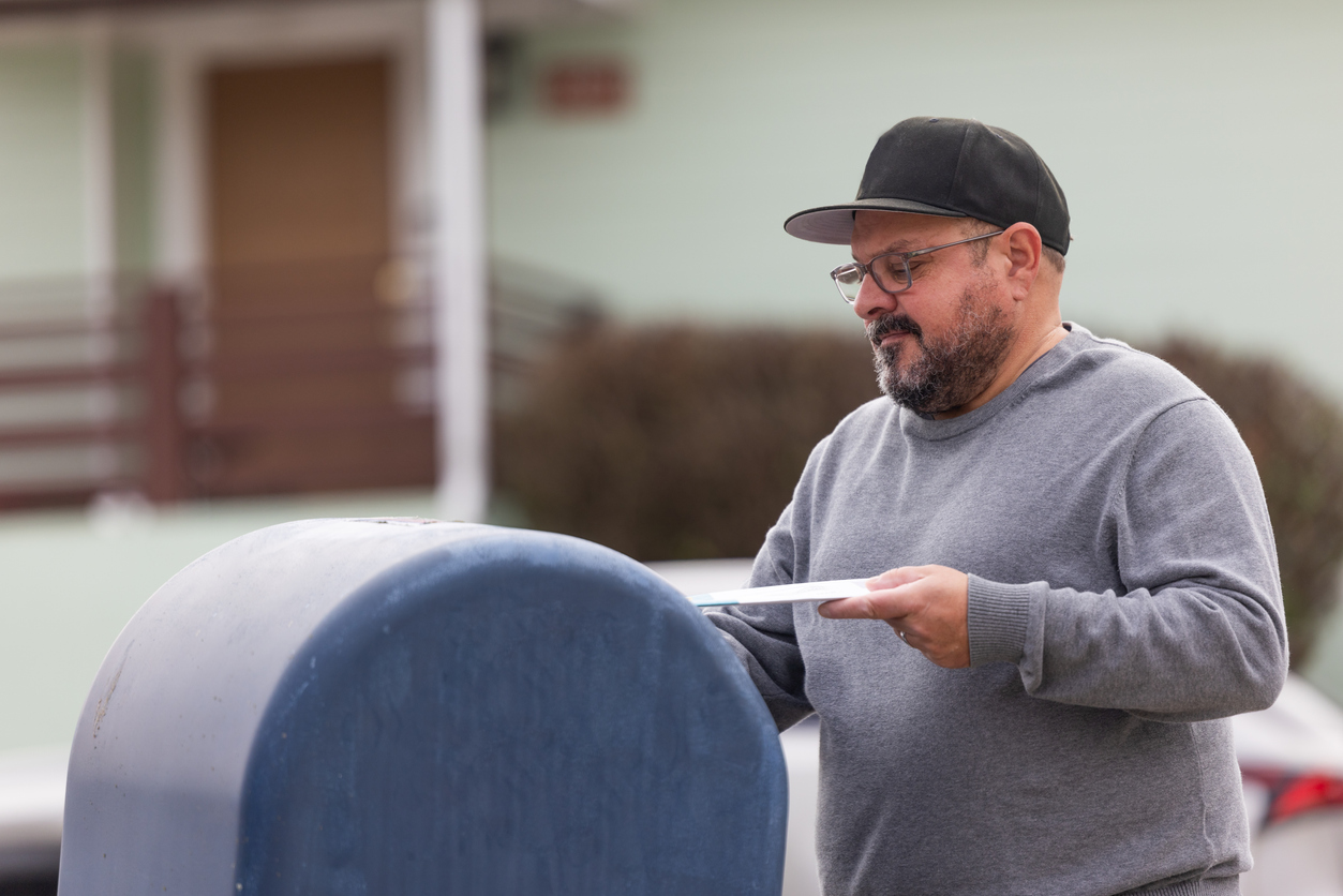 A man placing an envelope in a mailboc