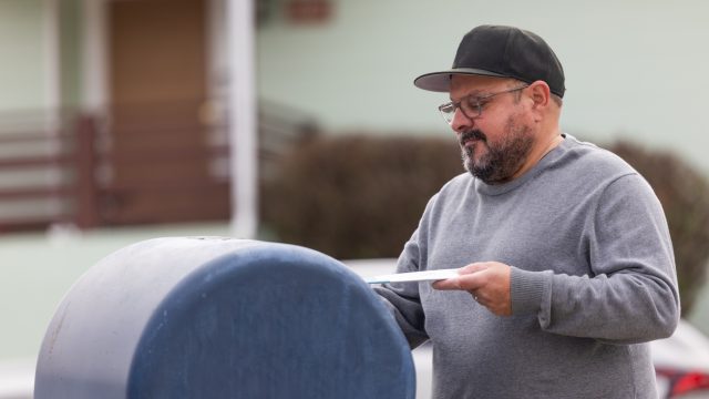 A man placing an envelope in a mailboc