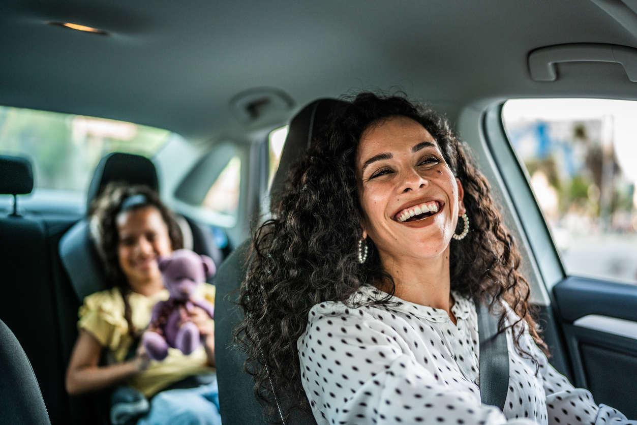A woman driving and smiling with a child sitting in the back seat