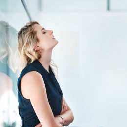frustrated-looking woman leaning against a glass wall sighing