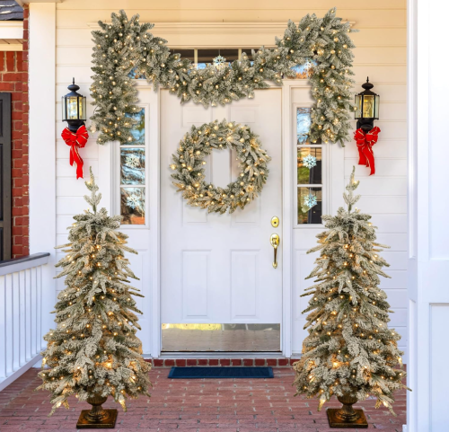 front door with christmas wreath, garland, and decorative trees