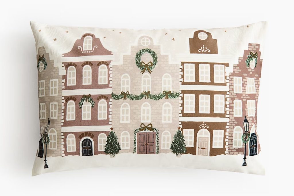 A festive Christmas pillow with a holiday street scene printed on it