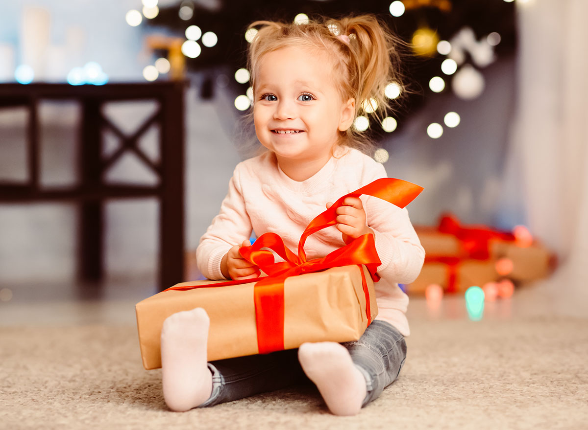 Christmas Eve. Curious little girl opening xmas gift at home, free space