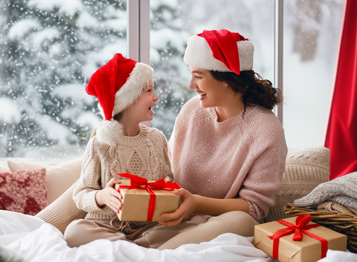 Merry Christmas and Happy Holidays. Cheerful mom and her cute daughter girl exchanging gifts. Parent and little child having fun near tree indoors. Morning Xmas.