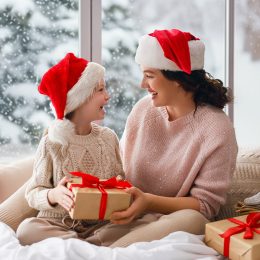 Merry Christmas and Happy Holidays. Cheerful mom and her cute daughter girl exchanging gifts. Parent and little child having fun near tree indoors. Morning Xmas.