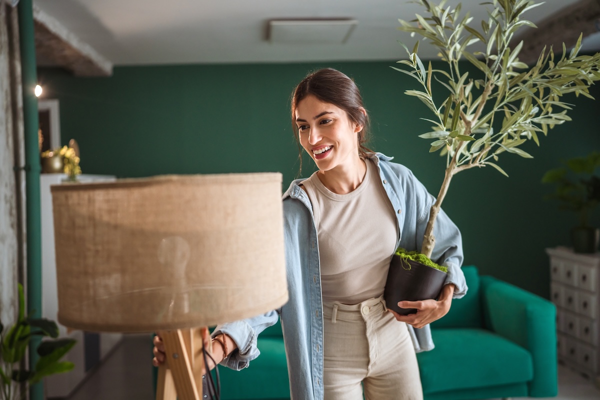 young woman arranging a lamp and a plant in a green room