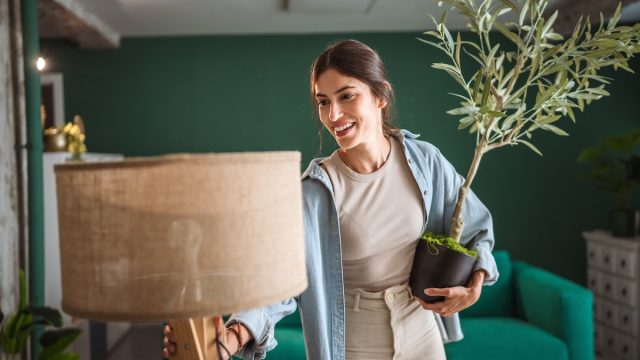 young woman arranging a lamp and a plant in a green room