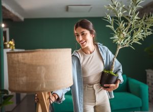 young woman arranging a lamp and a plant in a green room
