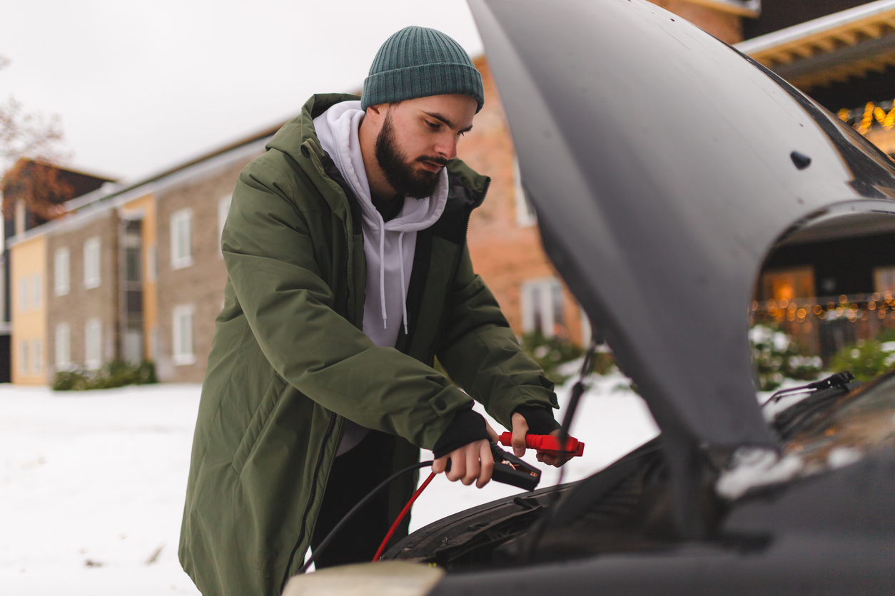 A man using jumper cables on his car during the winter