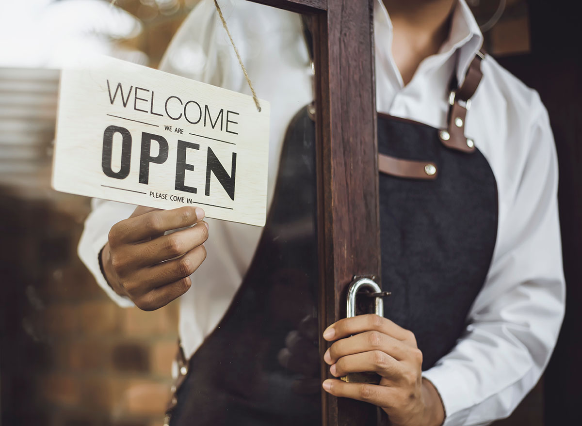 Store owner turning open sign broad through the door glass and ready to service.